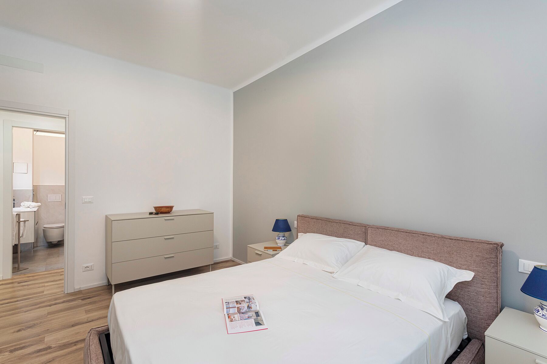 A bedroom with a bed, a nightstand, a dresser, and a door leading to a bathroom.