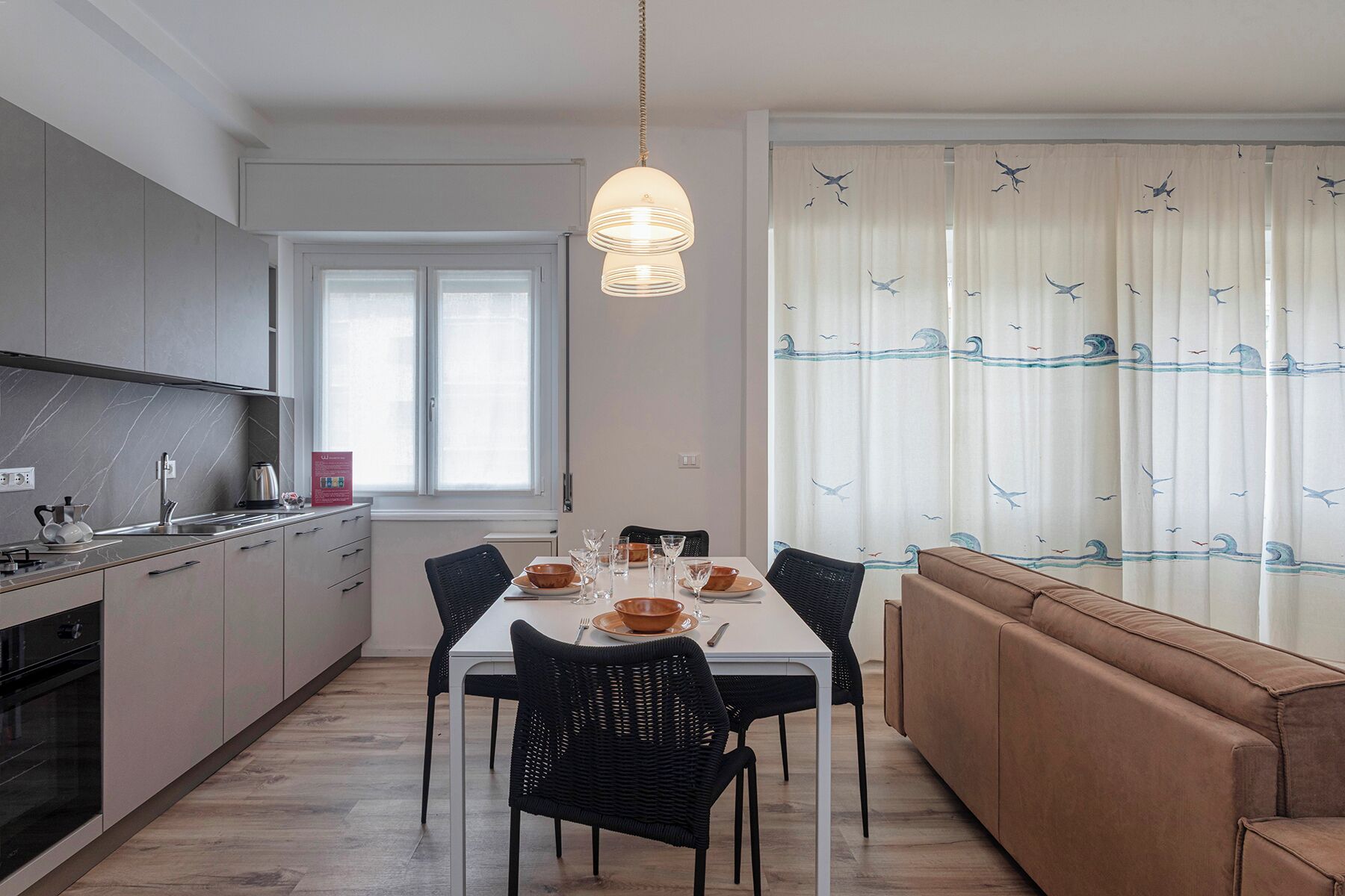 A modern kitchen with a dining area, a sofa, and a large window with curtains.