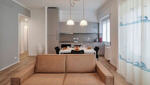 A modern kitchen with a dining area, featuring pendant lights, a sofa, and a view of the outdoors. - Quinto Modern Flat by Wonderful Italy (Genoa)