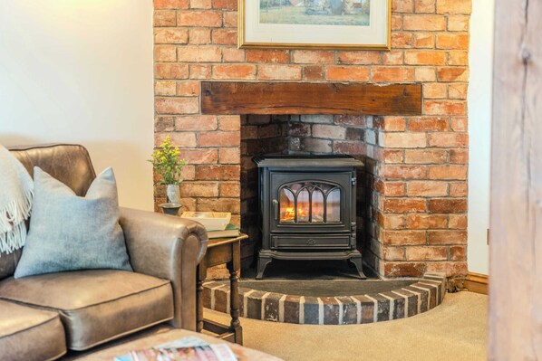 A cozy living room with a brick fireplace, a leather sofa, and a small table with a plant. - Poplar Cottage | Sleeps 3 | Near Broadway (Dumbleton)