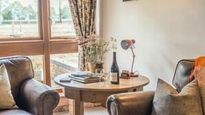 A cozy room with leather armchairs, a wooden table with a wine bottle, glasses, and a potted plant. - Poplar Cottage | Sleeps 3 | Near Broadway (Dumbleton)