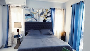 A bedroom with a large bed, a bedside table with a lamp, and a wall-mounted air conditioner. - Cozy 1-bedroom apartment in beautiful Grande Riviere with AC (Grande Riviere)