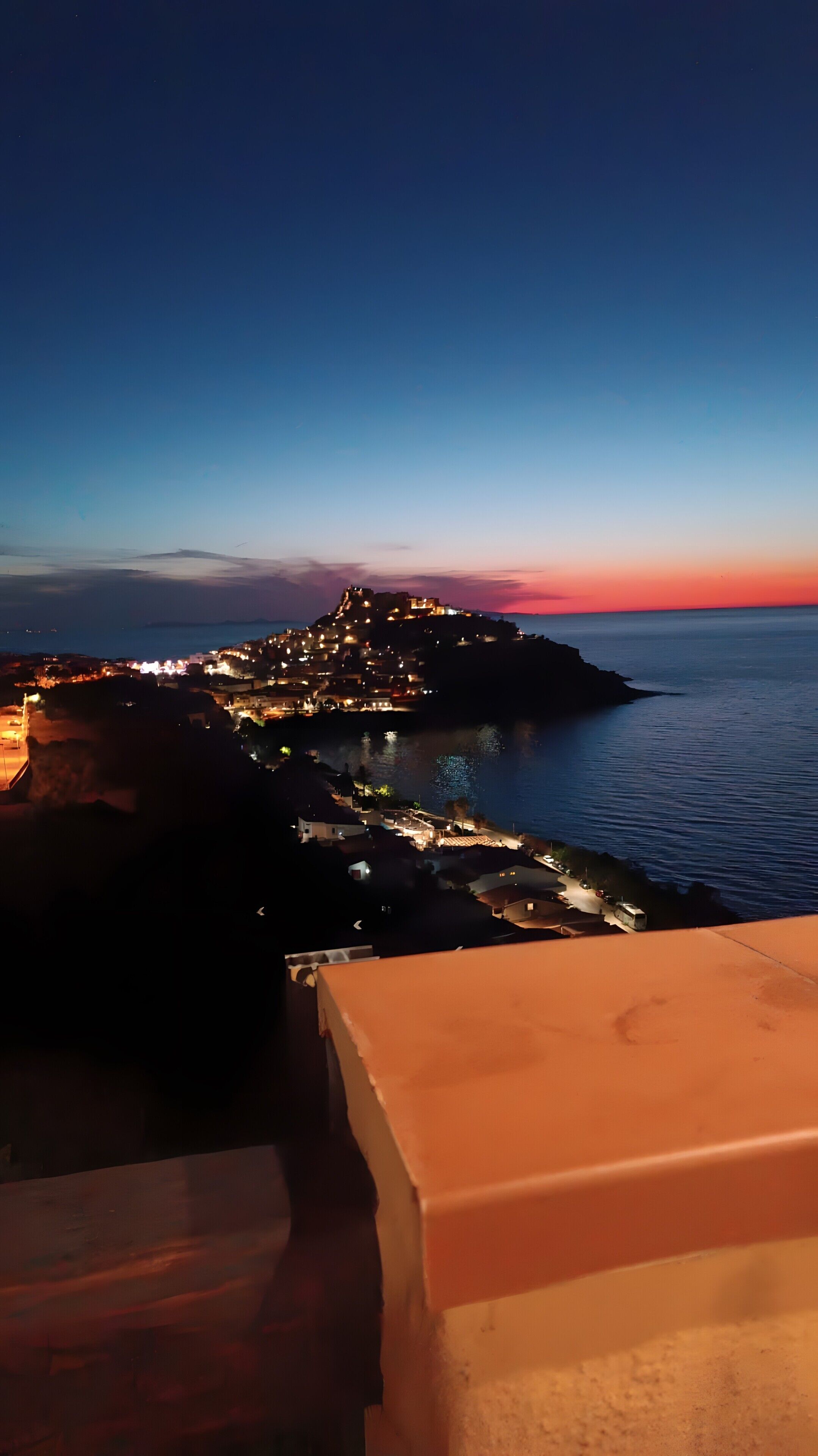 A coastal town at dusk with illuminated buildings and a view of the sea.