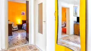 A hallway with a stone floor, a bed with a colorful blanket, a chair, and a lamp. - Apartment 'Maria- Castelsardo' with Mountain View, Wi-Fi and Air Conditioning (Castelsardo)