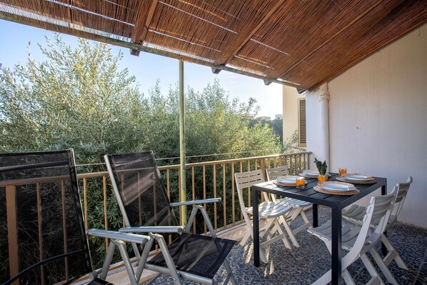 A balcony with a table set for two, chairs, and a view of greenery.