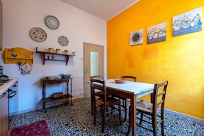 A dining area with a table and chairs, a kitchen area with a stove and cabinets, and a wall with decorative plates and paintings.