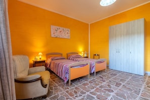 A room with two beds, a chair, a wardrobe, and a painting on the wall.
