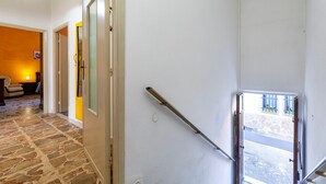 A hallway with a stone floor, a door leading to a room with a yellow wall, and a window with a view of the street. - Apartment 'Maria- Castelsardo' with Mountain View, Wi-Fi and Air Conditioning (Castelsardo)