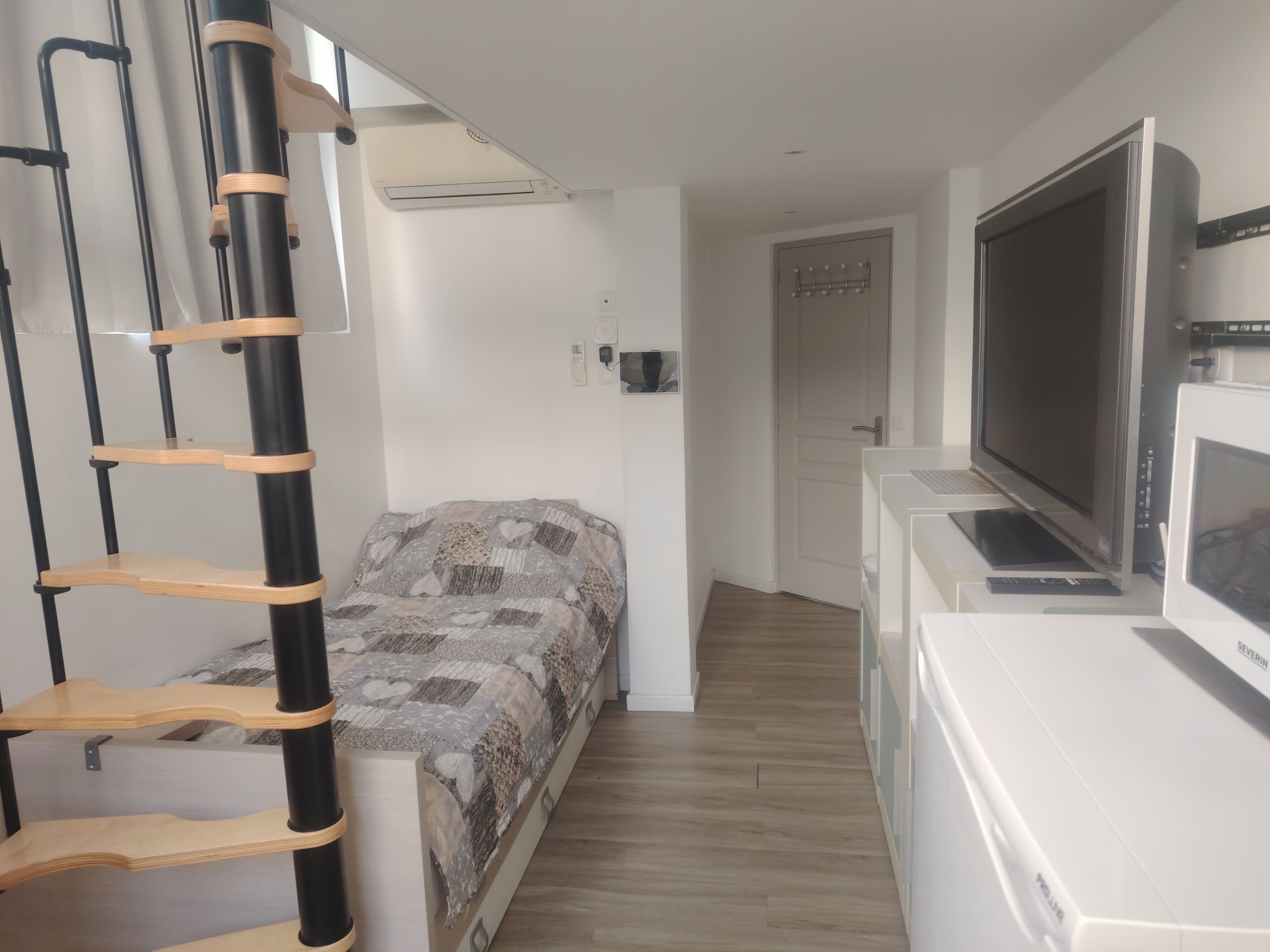 Una habitación pequeña con cama, televisión, escritorio y una escalera.