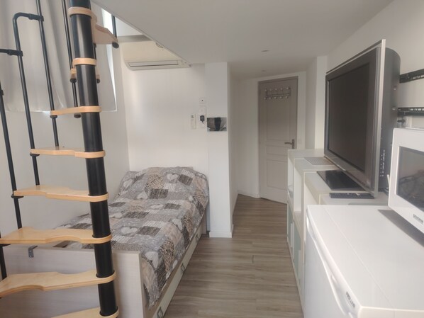 A compact room with a bed, a TV, a desk, and a ladder.