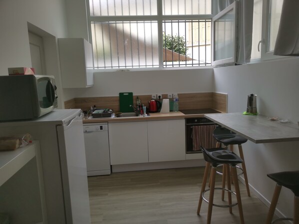 A compact kitchen with white cabinets, a microwave, a sink, and a coffee maker. There are two stools and a window with bars. - Perpignan Appart 5 mns Centre, Palais Congrès et Exposition 5 people (5 Beds) (Perpignan)