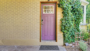 Une porte violette avec une petite fenêtre, un mur de briques et une vigne verte qui grimpe le long du mur.