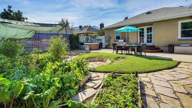 Un jardin avec un chemin en pierre, une terrasse en bois et un espace patio aménagé avec une table et des chaises.