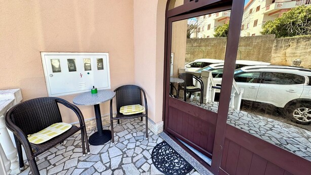 Un patio con due poltrone in vimini, un tavolino rotondo e una porta che si affaccia sulla strada.