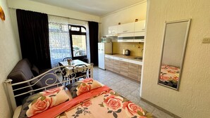 Una camera da letto con un letto, un comodino, una finestra con tende, un angolo cottura con armadietti e un forno a microonde, e un bagno con uno specchio.