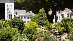 A garden with a pond, surrounded by various plants and trees, with white houses in the background. - Crafts Inn, Hotel Suite with pool and hot tub. (Wilmington)
