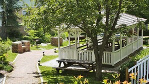 A gazebo with a wooden bench, surrounded by a garden with flowers and a brick structure in the background. - Crafts Inn, Hotel Suite with pool and hot tub. (Wilmington)