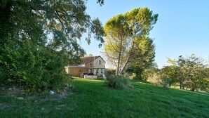 A house with a stone facade, surrounded by a well-maintained lawn and trees. - Pech Chabrol: Family Cottage with Pool and Vineyard View (Ribagnac)