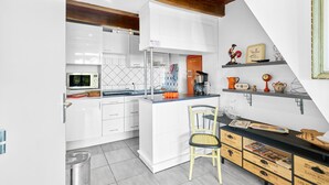 A modern kitchen with white cabinetry, a wooden ceiling, and a small island with a chair. - Pech Chabrol: Family Cottage with Pool and Vineyard View (Ribagnac)