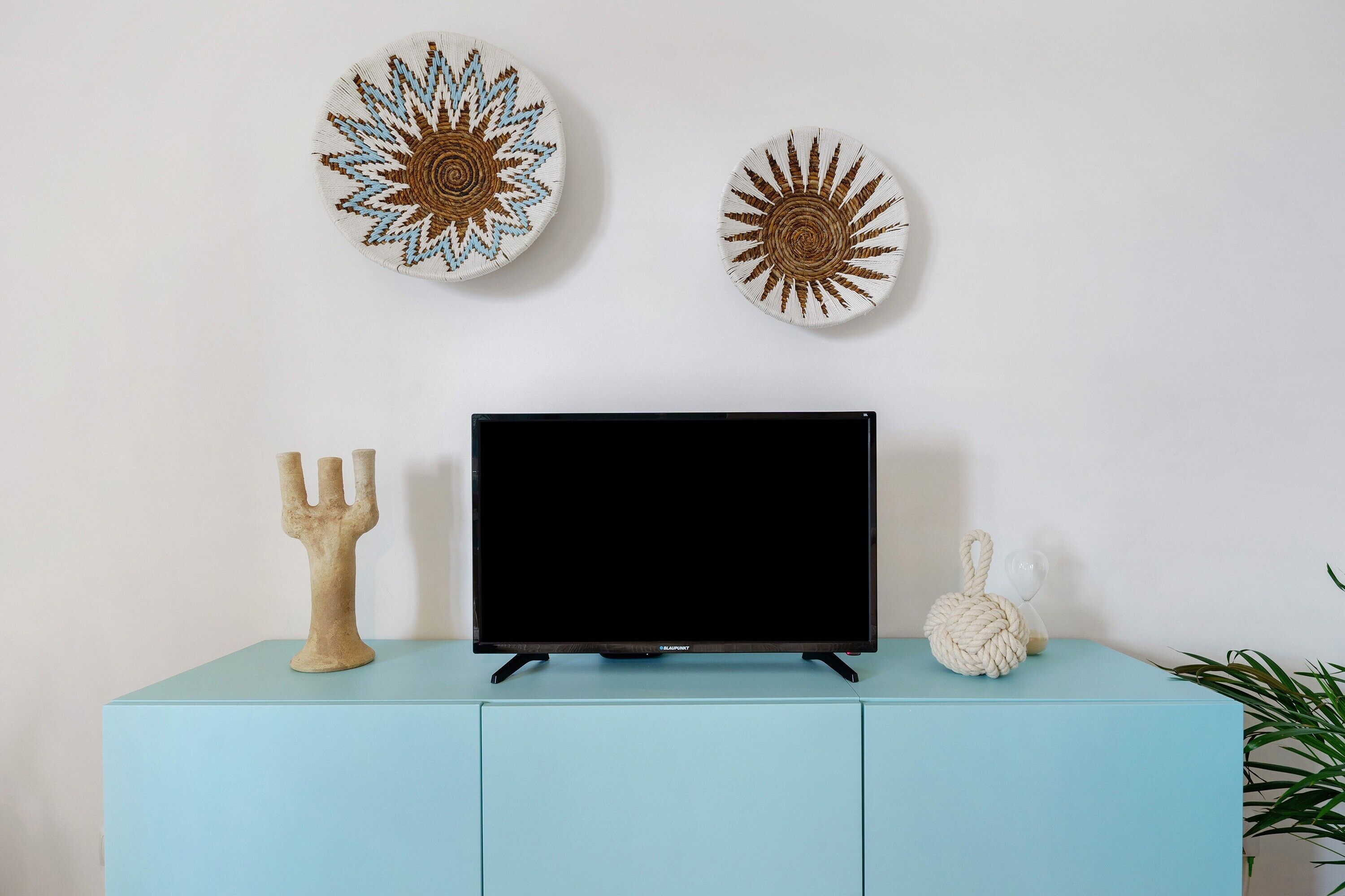 Ein Fernseher auf einem hellblauen Schrank mit dekorativen Tellern und einem Kandelaber.