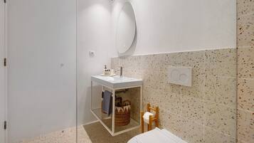 Une salle de bain avec un lavabo blanc, un miroir, un porte-serviettes, une petite chaise en bois et un panier décoratif.