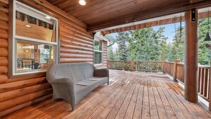 Eine Holzterrasse mit einer Rattan-Couch, Holzgeländern und Blick auf Bäume.