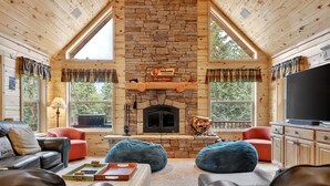 Ein gemütliches Blockhaus-Interieur mit Kamin aus Stein, Ledersofas und großen Fenstern mit Blick ins Freie.