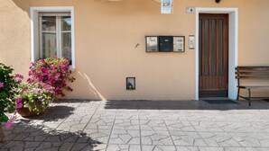 En bygnings facade med et træskilt der siger 'Agritur Vento Alpino', en dør, en bænk og en potteplante med blomster.
