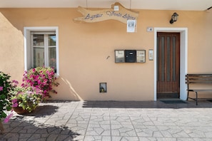 Une façade d’immeuble avec une enseigne en bois indiquant « Agritur Vento Alpino », une porte, un banc et un pot de fleurs.