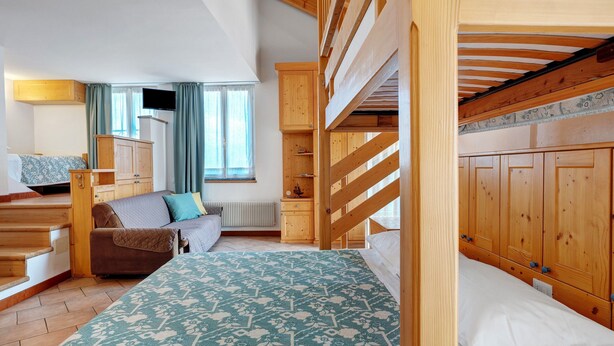 A room with bunk beds, a sofa, a small table, and a cabinet. - Room 'Vento Alpino Campanile' with Balcony and Wi-Fi (Coredo)