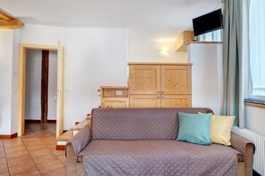 Un salon avec un canapé, des meubles en bois, un téléviseur et une fenêtre avec des rideaux.