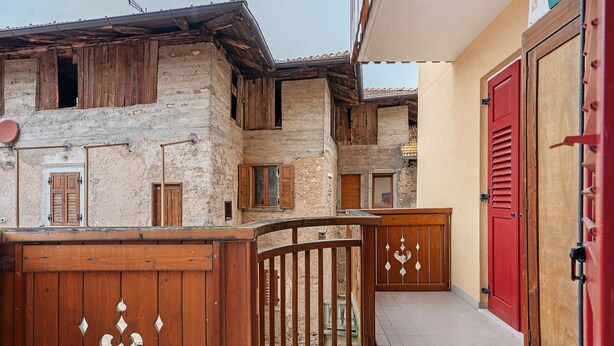 A courtyard with a wooden fence, a red door, and a building with a stone facade. - Apartment 'Gianni' with Mountain View, Balcony and Wi-Fi (Coredo)