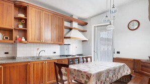 A kitchen with wooden cabinets, a stove, and a dining table with a floral tablecloth. - Apartment 'Gianni' with Mountain View, Balcony and Wi-Fi (Coredo)