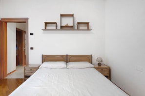 Ein Schlafzimmer mit einem hölzernen Bett, Nachttischen, einem Beistelltisch und einem an der Wand befestigten Regal mit Spiegel und Dekoration.
