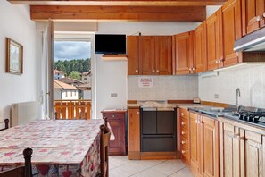 Cocina pequeña con armarios de madera, horno empotrado y televisor sobre la encimera.