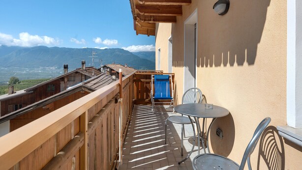 Ein Balkon mit Blick auf Berge, einem Hollerleger, einem Tisch mit Stühlen und einem blauen Stuhl.
