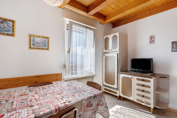 A bedroom with a bed, a table, a TV, a wardrobe, and a window with curtains.