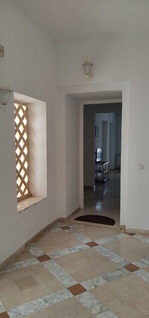 A hallway with a tiled floor, a door leading to another room, and a light fixture on the ceiling.