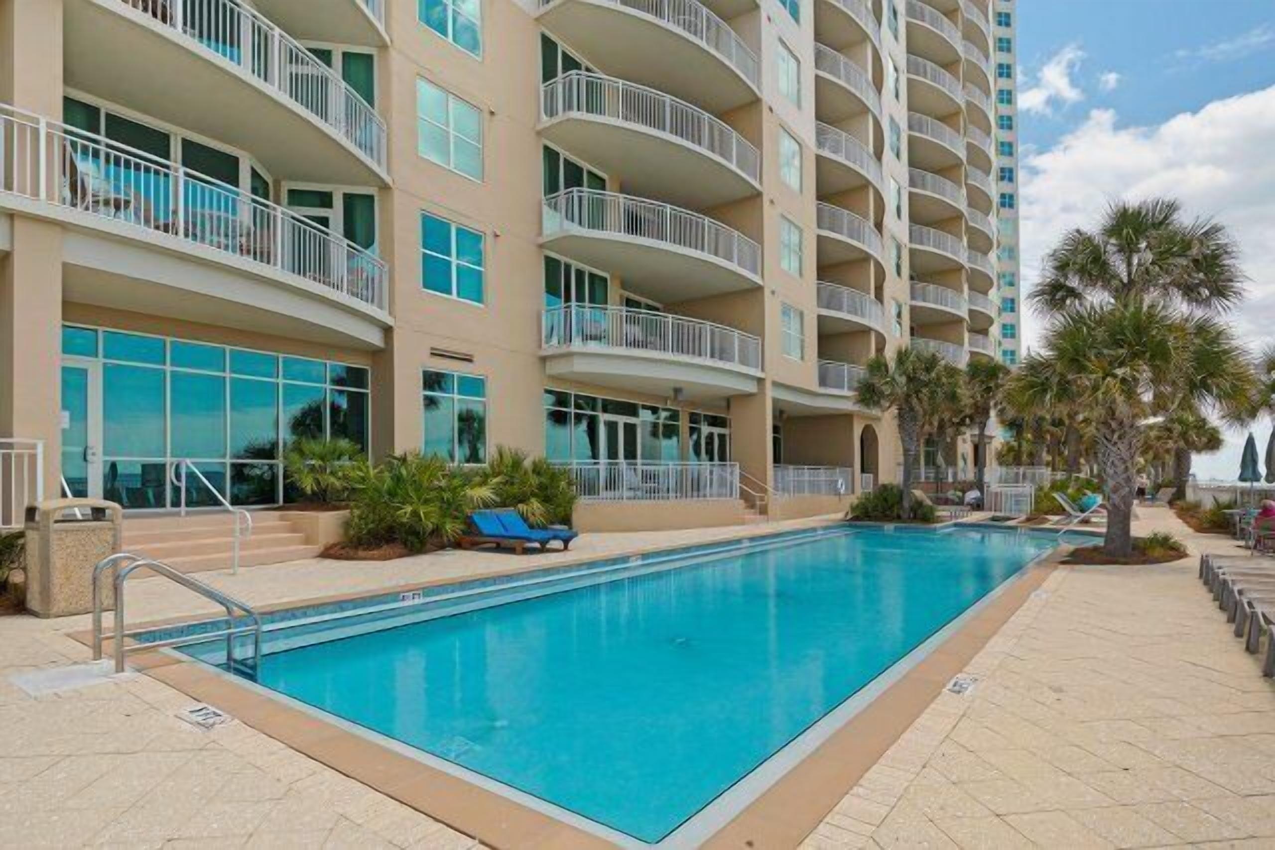 A hotel with a swimming pool, multiple balconies, and palm trees.