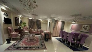 A spacious living room with a large coffee table, sofas, a TV, and a dining area with purple chairs. - Sea view in gleem luxury apartments - Saba Basha - alexandria (Alexandria)
