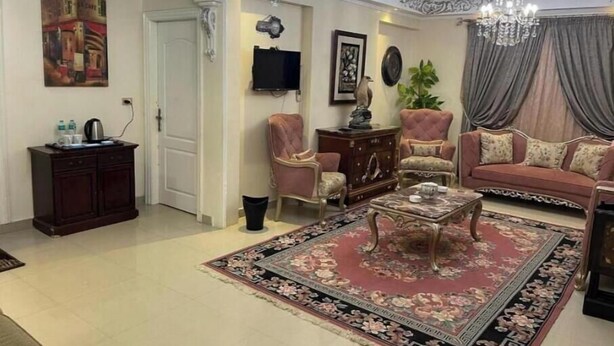 A living room with a sofa, armchairs, a coffee table, a TV, and a chandelier. - Sea view in gleem luxury apartments - Saba Basha - alexandria (Alexandria)
