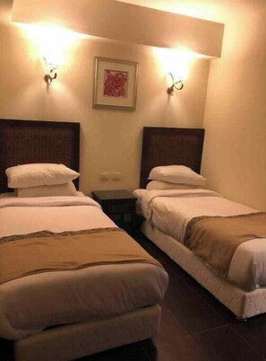Een hotelkamer met twee eenpersoonsbedden, een nachtkastje en een ingelijst foto aan de muur.