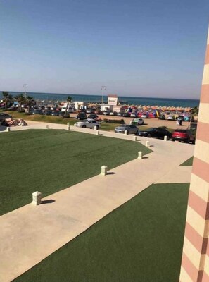 A beachside parking area with a clear view of the ocean, a postal service sign, and a grassy area. - Sea view,chalet in Porto south beach,el sokhna 2BR (Alexandria)