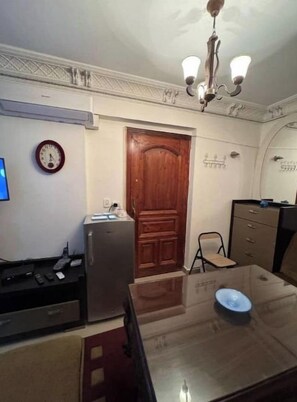 A dining area with a wooden table, chairs, a clock, a refrigerator, and a chandelier. - Amazing studio apartment gleem (Alexandria)