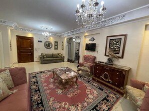 A spacious living room with a chandelier, a sofa set, a coffee table, and a TV.