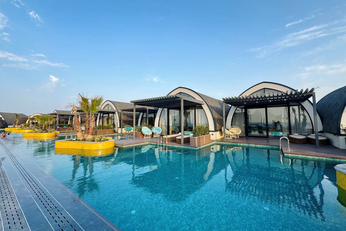 Zona de piscina con arquitectura moderna y curvas, y mobiliario exterior.