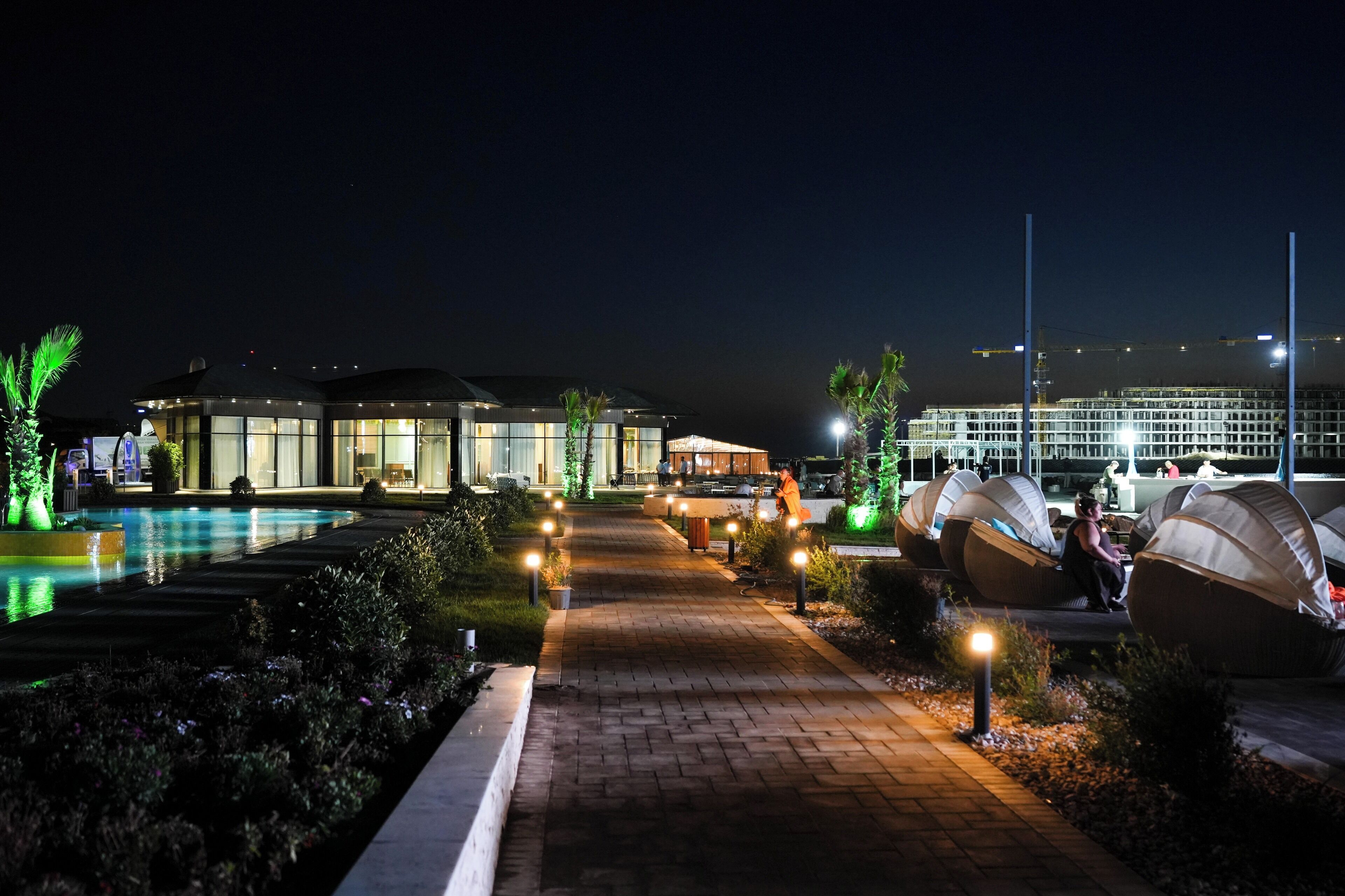 A well-lit outdoor area with a swimming pool, lounge chairs, and a building with large windows.
