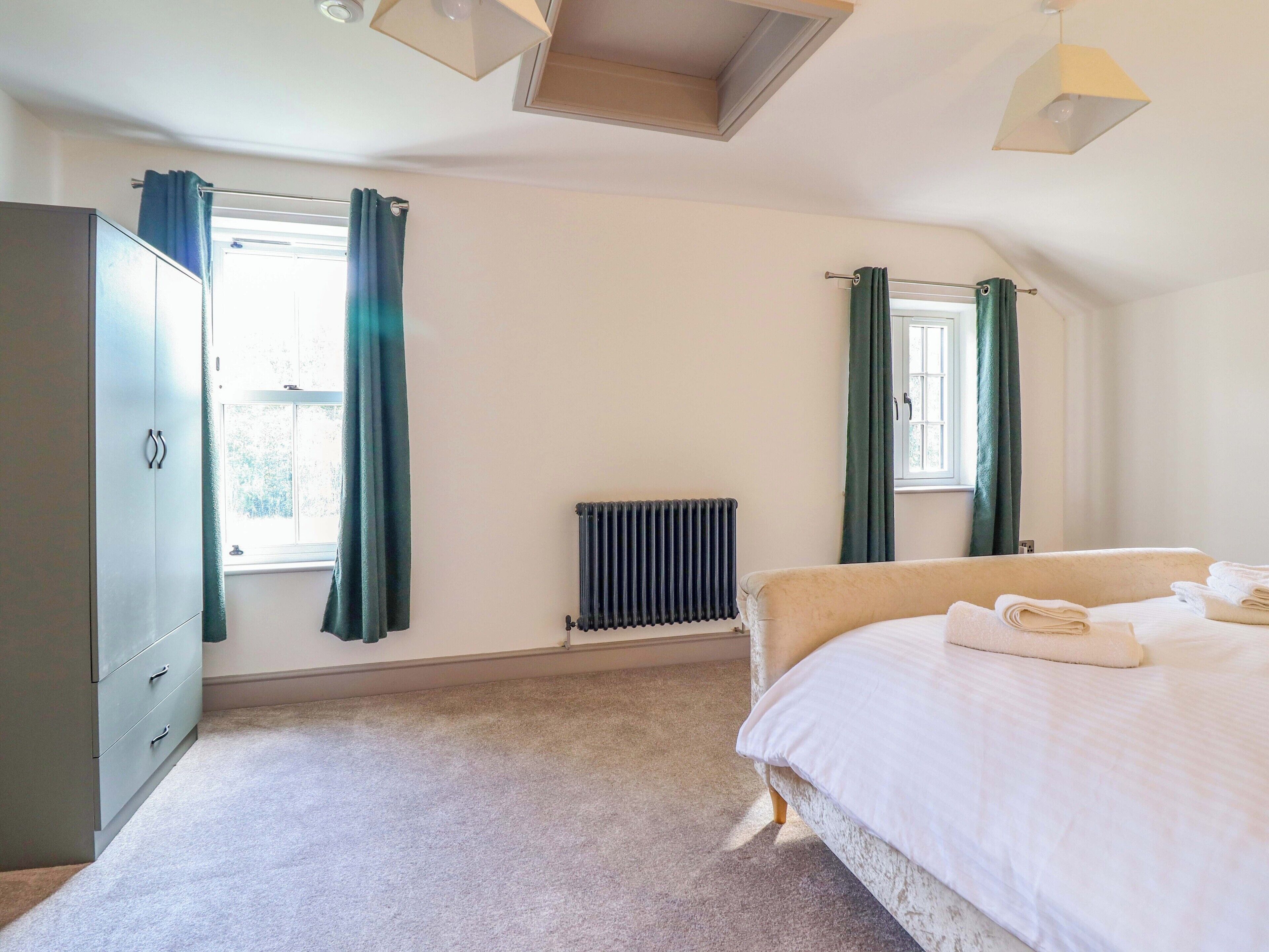 Ein Schlafzimmer mit Bett, Heizkörper, einem Fenster mit Vorhängen und einem Kleiderschrank.