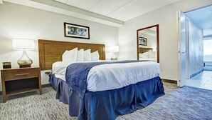 Una habitación de hotel con cama, mesitas de noche, lámparas, un reloj, un cuadro en la pared y un espejo.