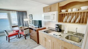 Una cocina compacta con microondas, cafetera y lavamanos. Hay una zona de comedor con mesa y sillas, y un televisor sobre un escritorio.